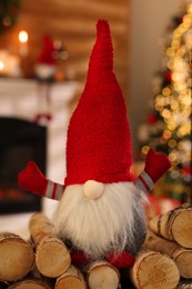 Cute Christmas gnome on firewood in room with festive decorations