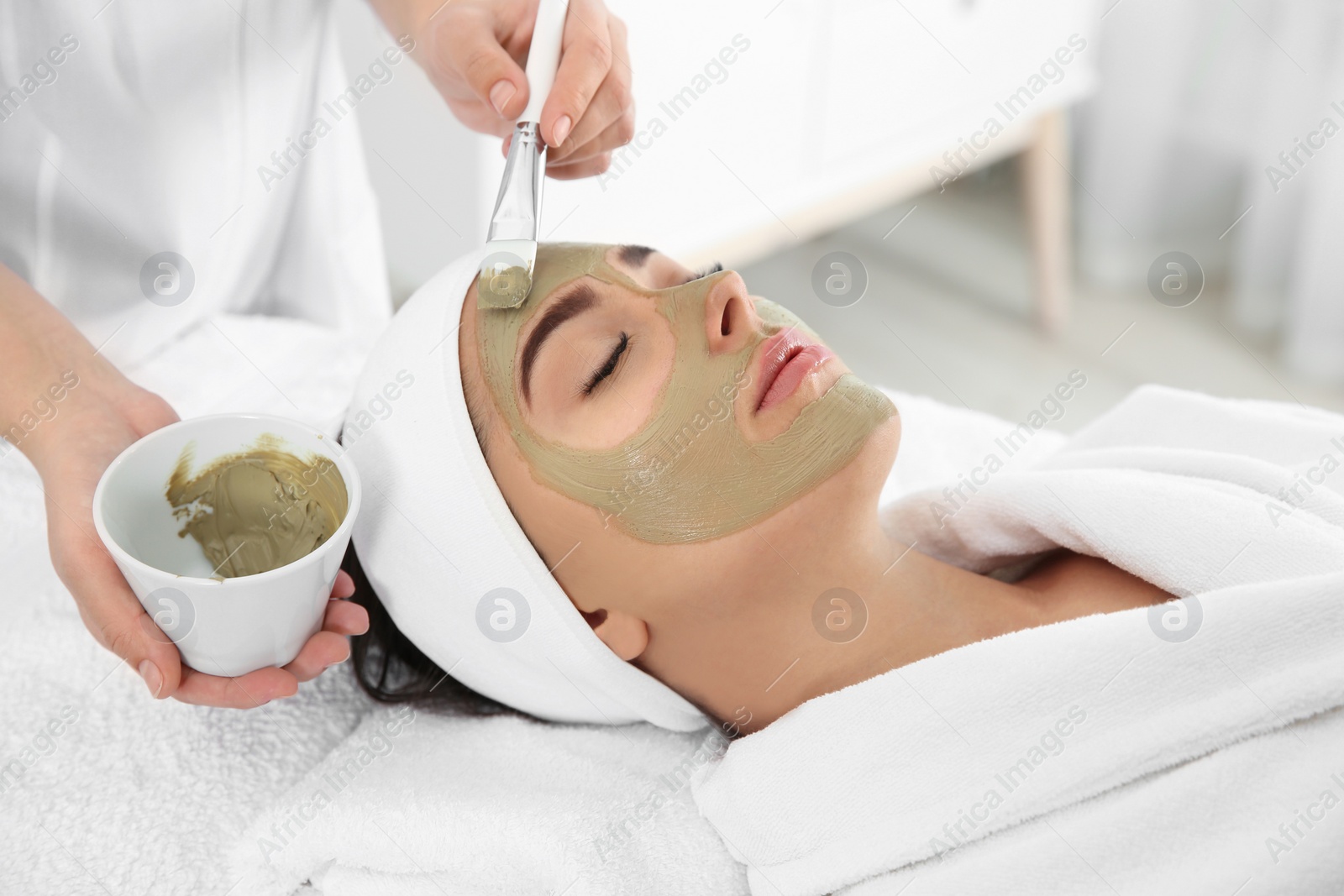 Photo of Cosmetologist applying mask on client's face in spa salon