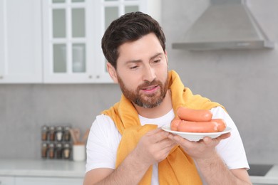 Man holding plate with sausages in kitchen