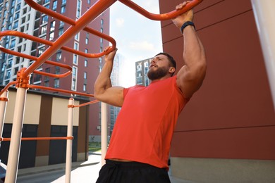 Photo of Man training on horizontal bars at outdoor gym on sunny day
