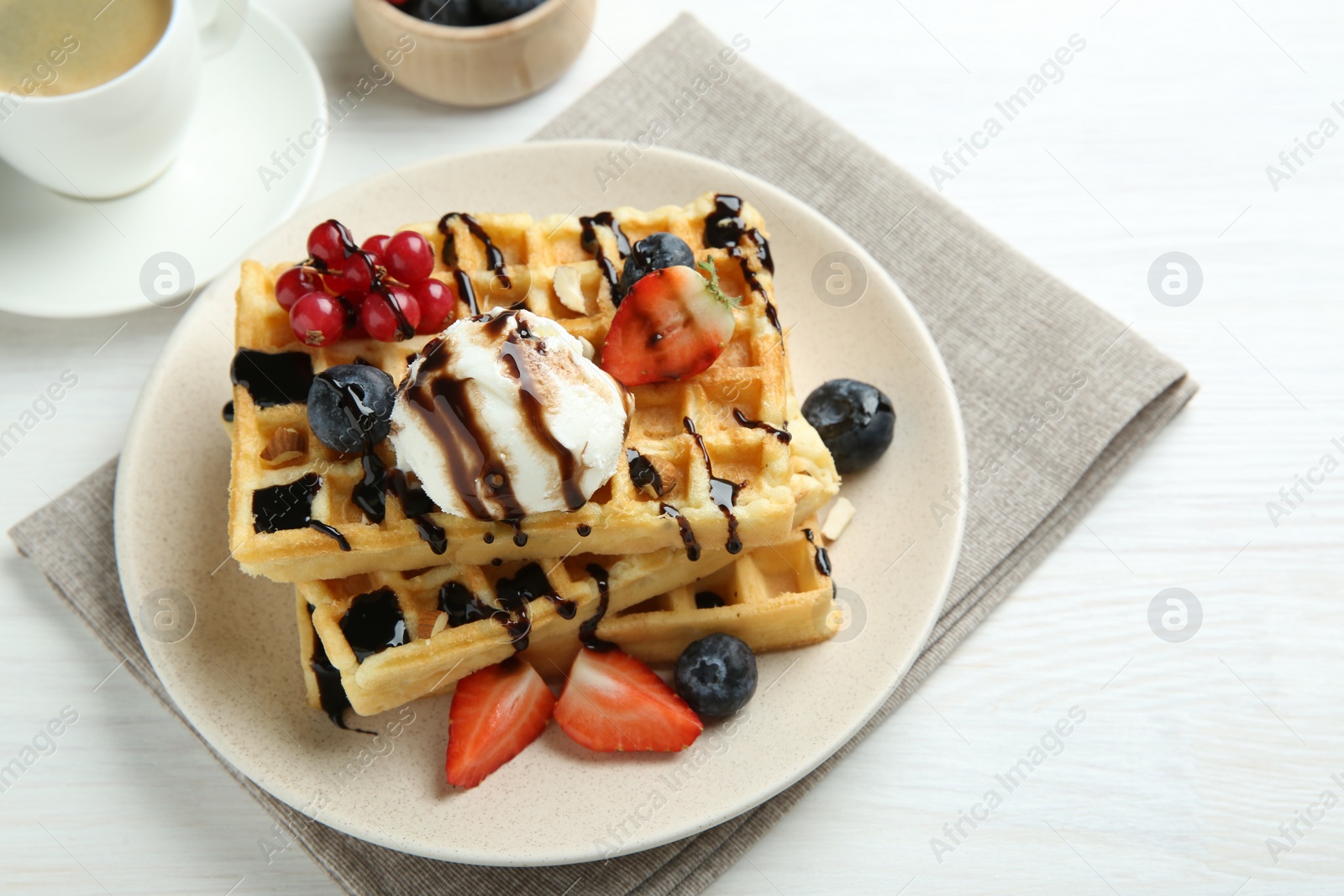 Photo of Delicious Belgian waffles with ice cream, berries and chocolate sauce served on white wooden table, closeup
