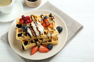 Delicious Belgian waffles with ice cream, berries and chocolate sauce served on white wooden table, closeup