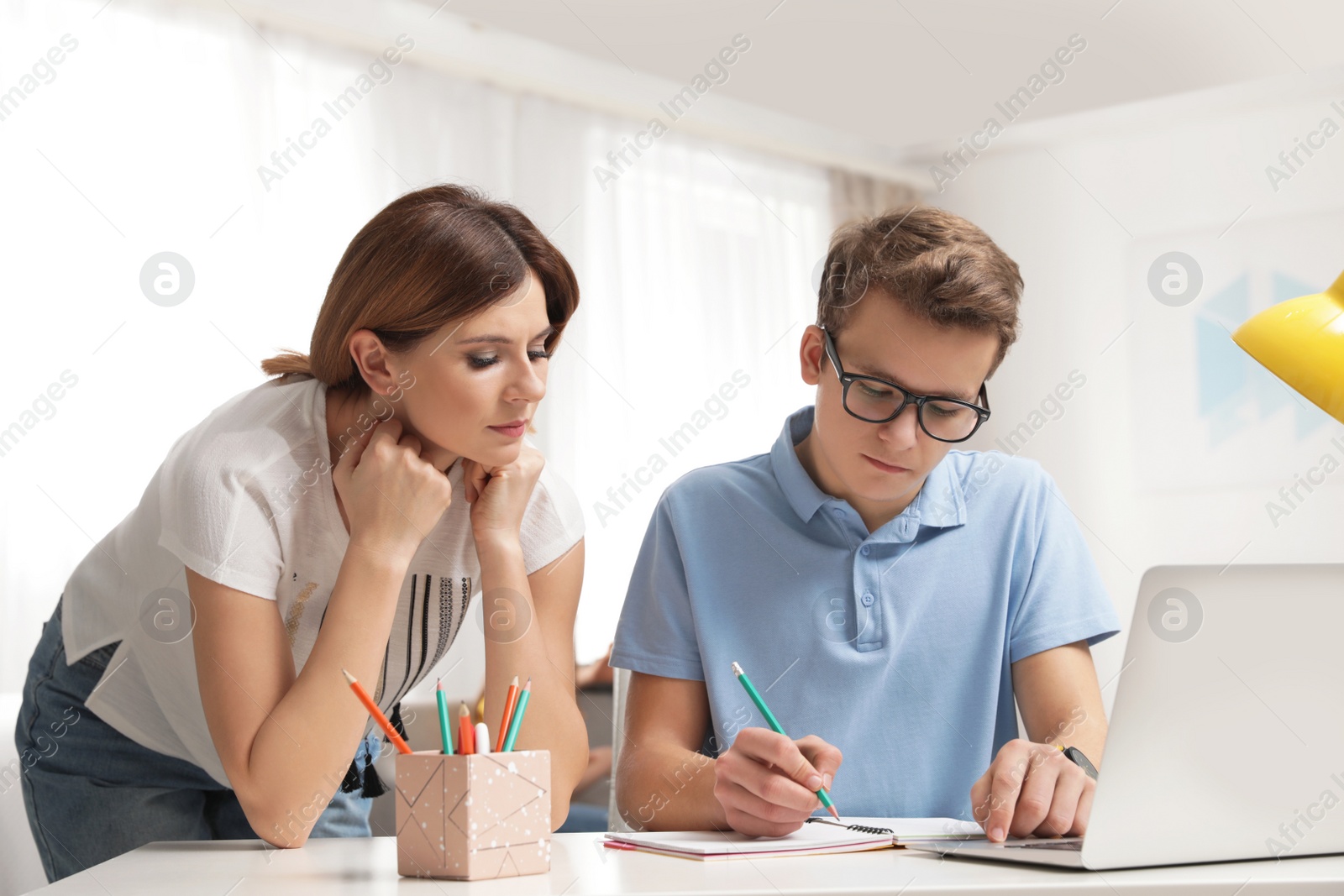 Photo of Mother helping her teenager son with homework indoors