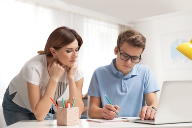 Photo of Mother helping her teenager son with homework indoors