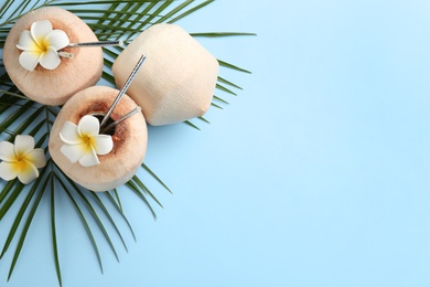 Fresh coconuts with drinking straws and flowers on light blue background, flat lay. Space for text