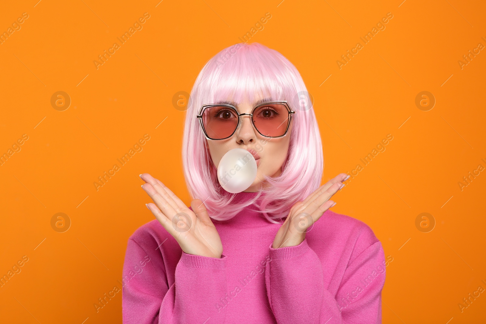 Photo of Beautiful woman in sunglasses blowing bubble gum on orange background