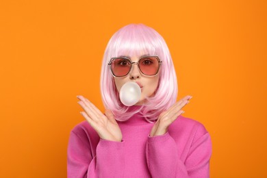 Beautiful woman in sunglasses blowing bubble gum on orange background