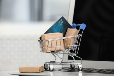 Photo of Online payment concept. Small shopping cart with bank card, boxes and laptop, closeup