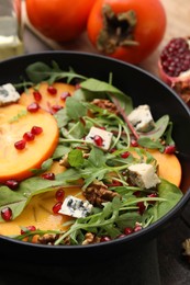 Photo of Tasty salad with persimmon, blue cheese, pomegranate and walnuts served on wooden table, closeup