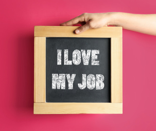 Employee engagement concept. Woman holding chalkboard with text I Love My Job on pink background, closeup