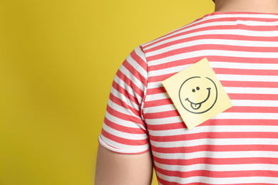 Man with funny face sticker on back against yellow background, closeup. April fool's day