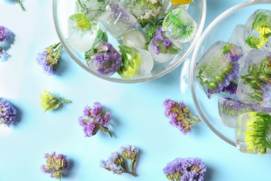 Photo of Ice cubes with flowers and glass bowls on blue background, flat lay