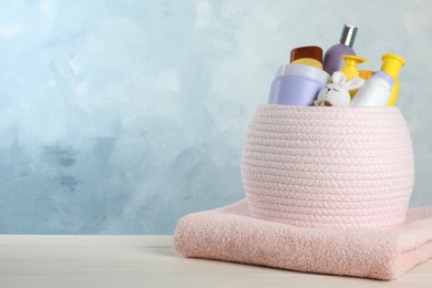 Photo of Basket with different baby cosmetic products, toy and towel on white wooden table. Space for text