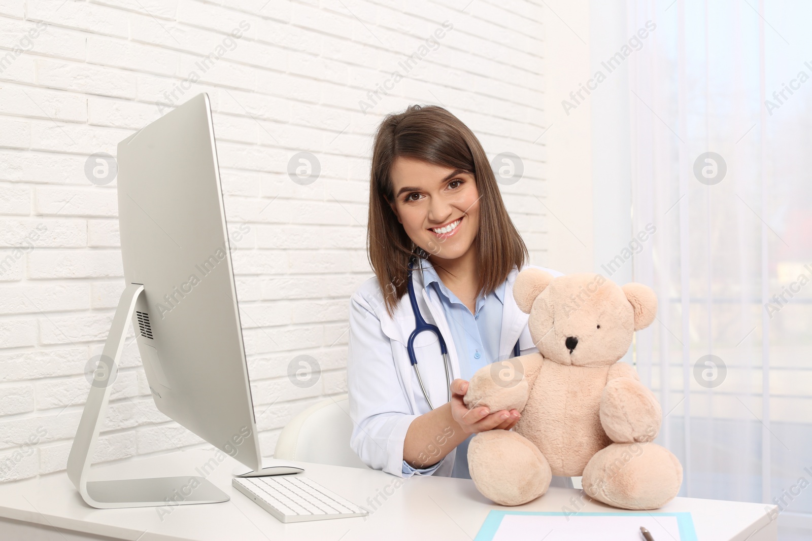 Photo of Pediatrician with teddy bear at table in clinic