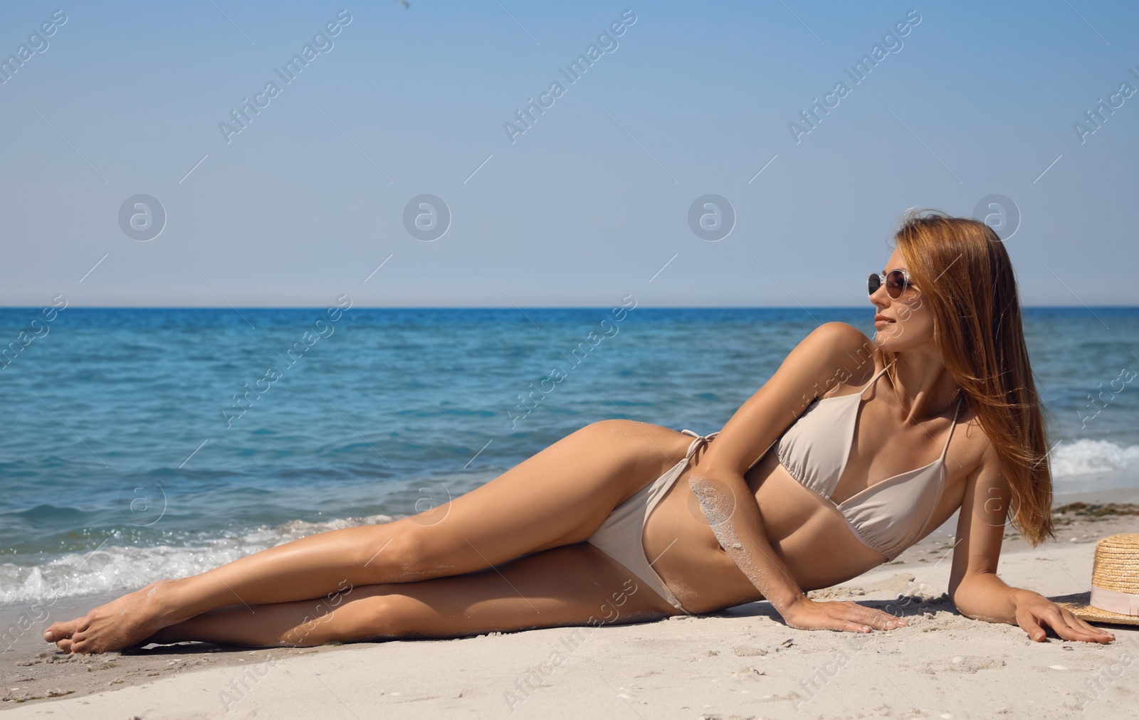 Photo of Attractive woman with perfect body in bikini lying on sandy beach near sea