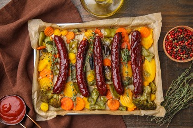 Baking tray with delicious smoked sausages and ingredients on wooden table, flat lay