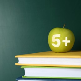 Image of Apple with carved number five and plus symbol as school grade on books near green chalkboard, space for text
