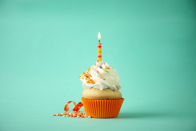 Photo of Delicious birthday cupcake with candle on light green background
