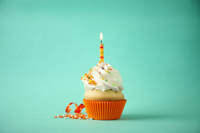 Delicious birthday cupcake with candle on light green background