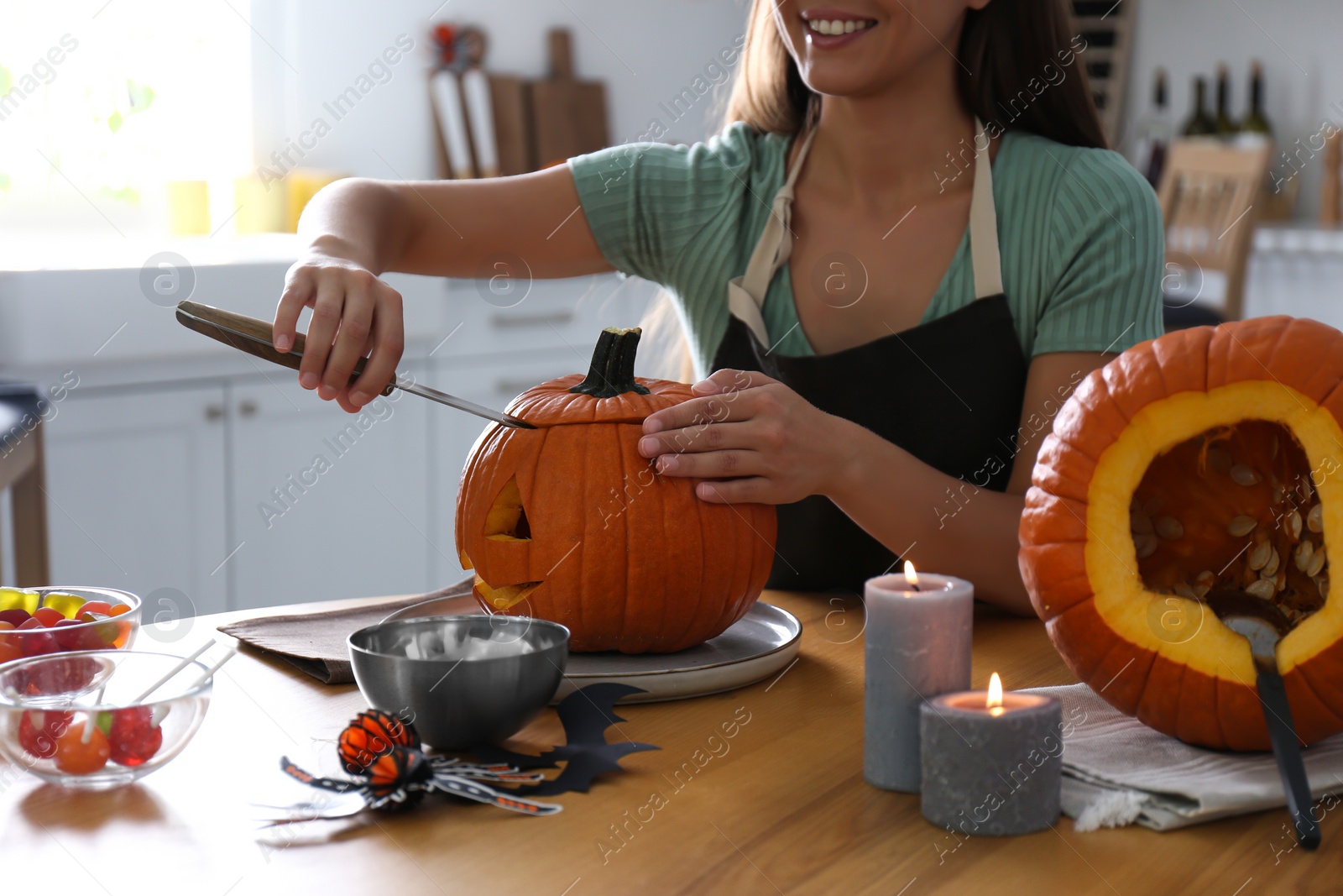 Photo of Woman making pumpkin jack o'lantern at table in kitchen, closeup. Halloween celebration