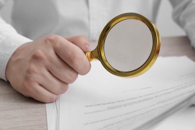Photo of Man looking at document through magnifier at white wooden table, closeup. Searching concept