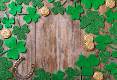Frame made of clover leaves and gold coins on wooden table, flat lay with space for text. St. Patrick's Day celebration
