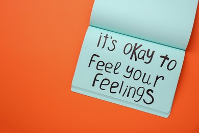 Photo of Notebook with phrase It`s Okay To Feel Your Feelings on orange background, top view. Space for text