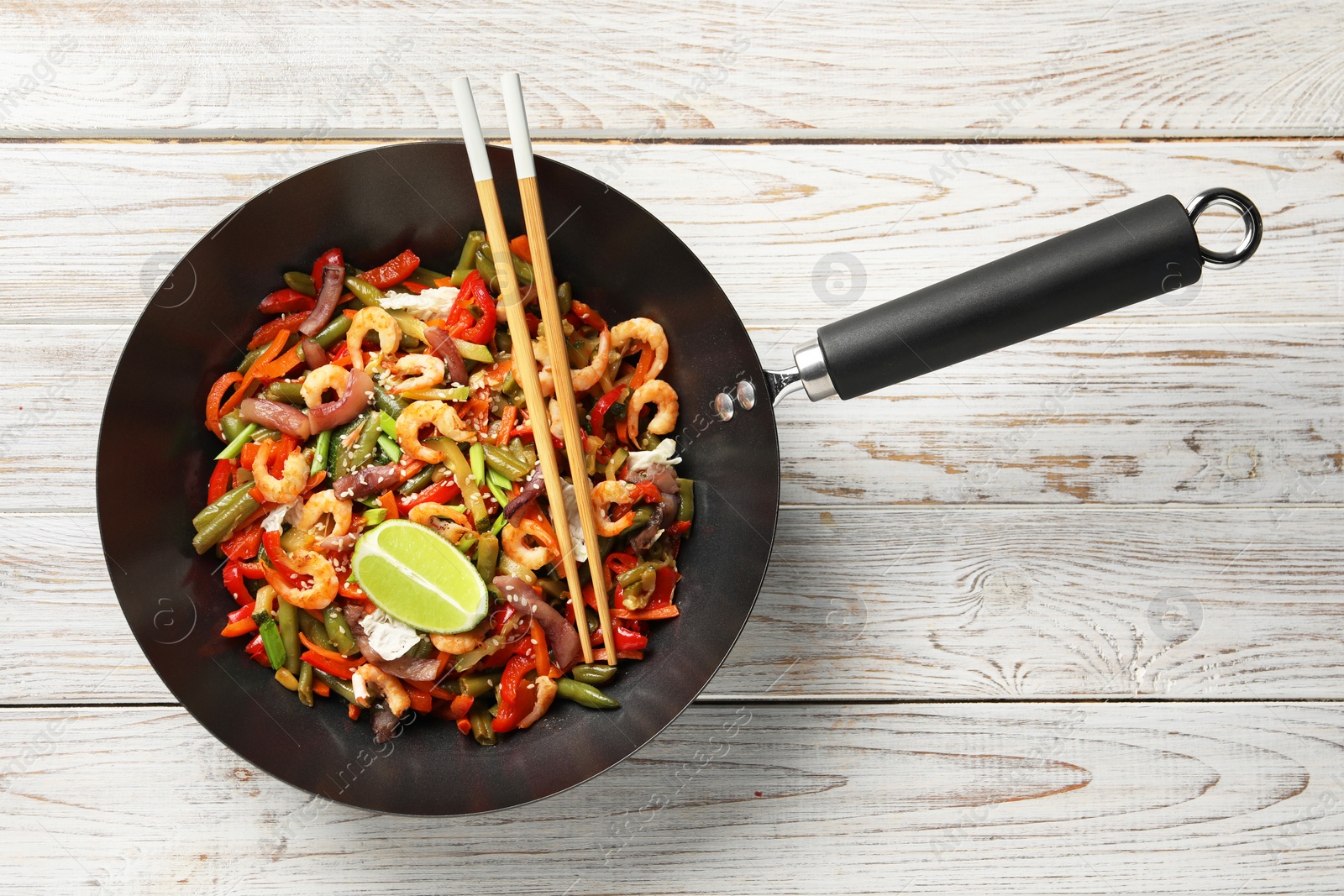 Photo of Shrimp stir fry with vegetables in wok and chopsticks on light wooden table, top view