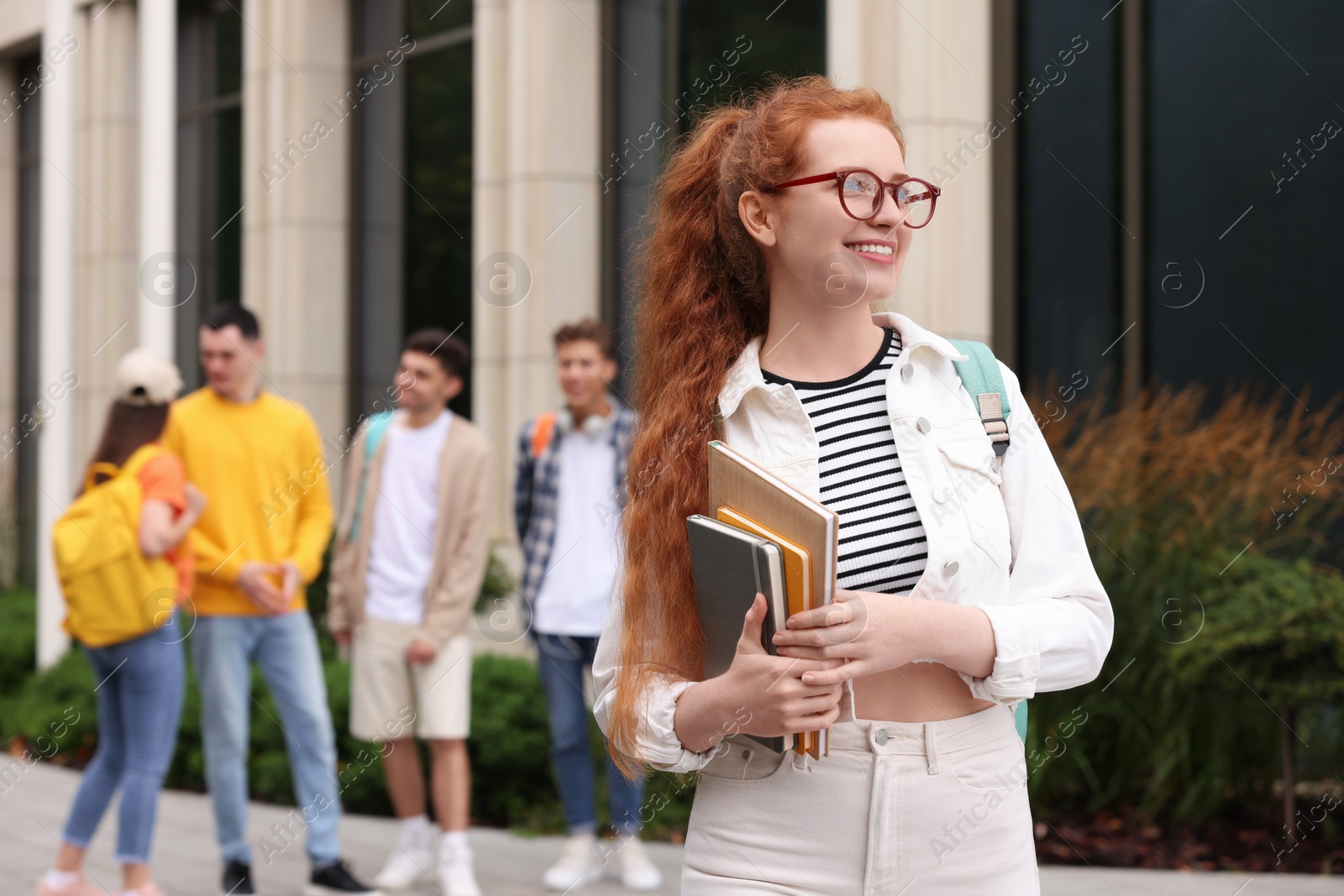 Photo of Students spending time together outdoors. Happy young woman with notebooks, selective focus