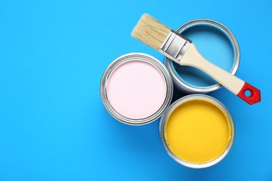 Photo of Cans of colorful paints and brush on light blue background, flat lay. Space for text