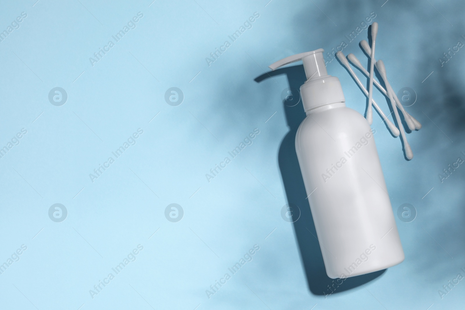 Photo of Bottle of face cleansing product and cotton buds on light blue background, flat lay. Space for text