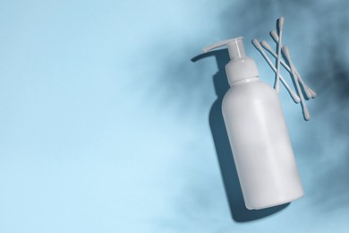 Bottle of face cleansing product and cotton buds on light blue background, flat lay. Space for text
