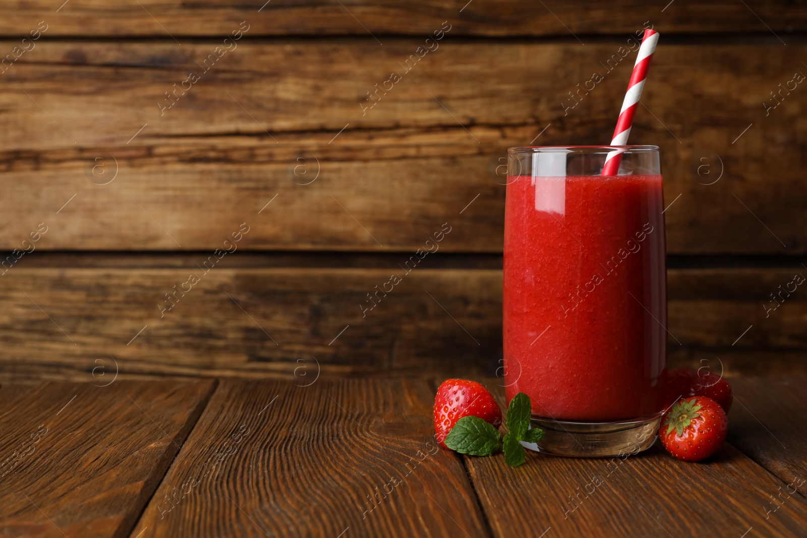 Photo of Glass with delicious strawberry smoothie on wooden table. Space for text