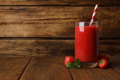 Photo of Glass with delicious strawberry smoothie on wooden table. Space for text