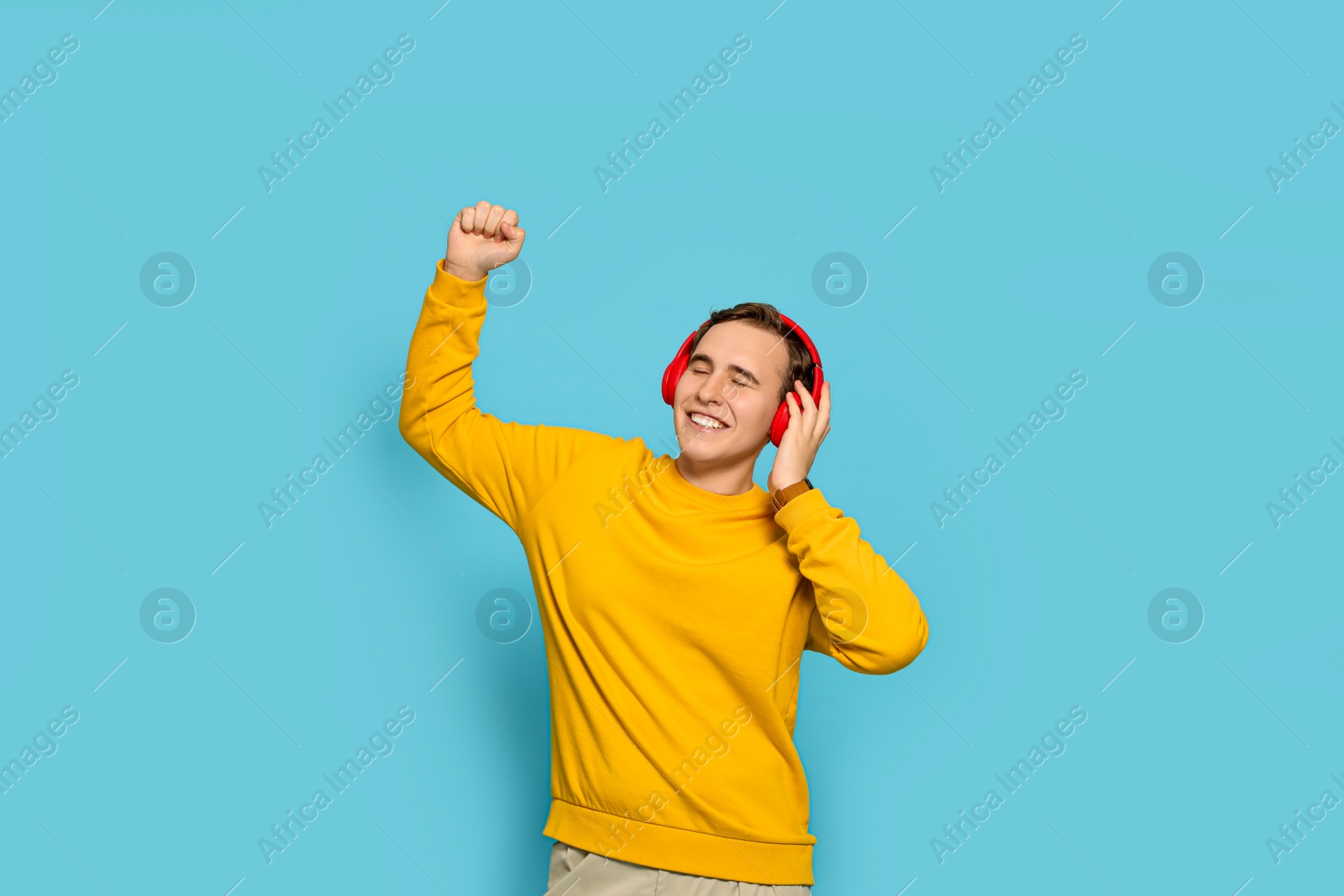 Photo of Handsome young man with headphones dancing on light blue background
