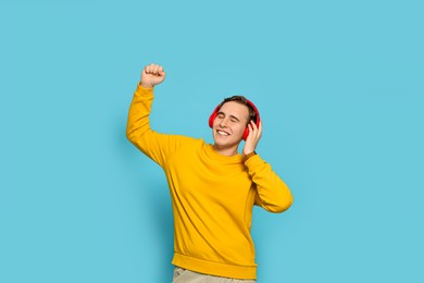 Handsome young man with headphones dancing on light blue background