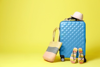 Stylish blue suitcase with beach accessories on yellow background. Space for text