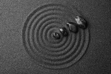Photo of Black sand with stones and beautiful pattern, flat lay. Zen concept