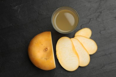 Glass of fresh natural turnip juice and cut root on black table, flat lay