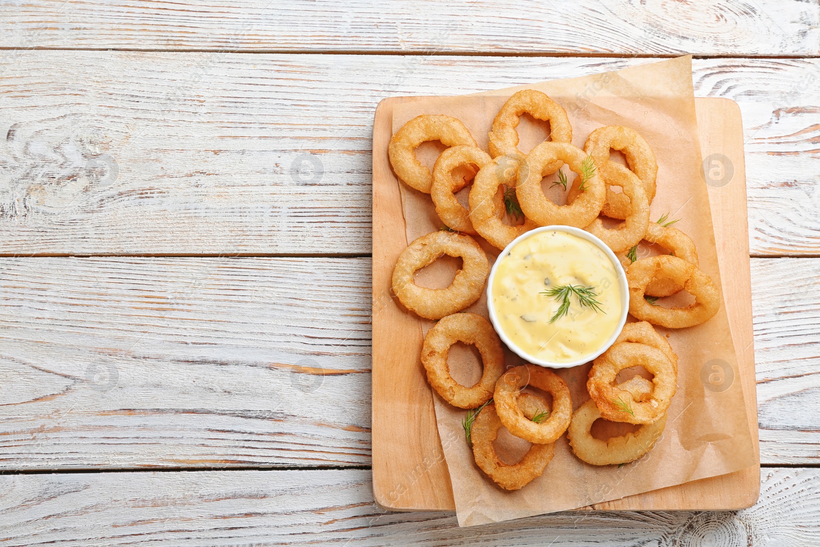 Photo of Fried onion rings served with sauce on wooden board, top view