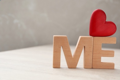 Photo of Phrase Love Me made of red heart and wooden letters on white table, closeup. Space for text