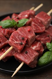 Photo of Wooden skewers with cut fresh beef meat, basil leaves and spices on table, closeup