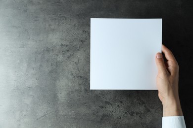 Man holding blank book at black textured table, top view. Mockup for design