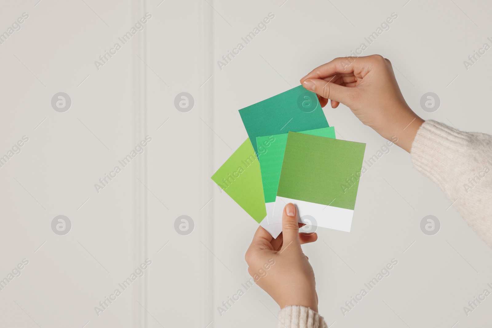 Photo of Woman with color sample cards choosing paint shade for wall indoors, closeup. Interior design