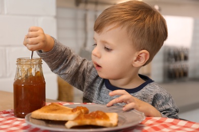 Photo of Little boy having breakfast with toast bread and jam at table in kitchen