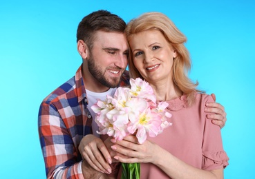 Photo of Young man congratulating his mature mom on color background. Happy Mother's Day