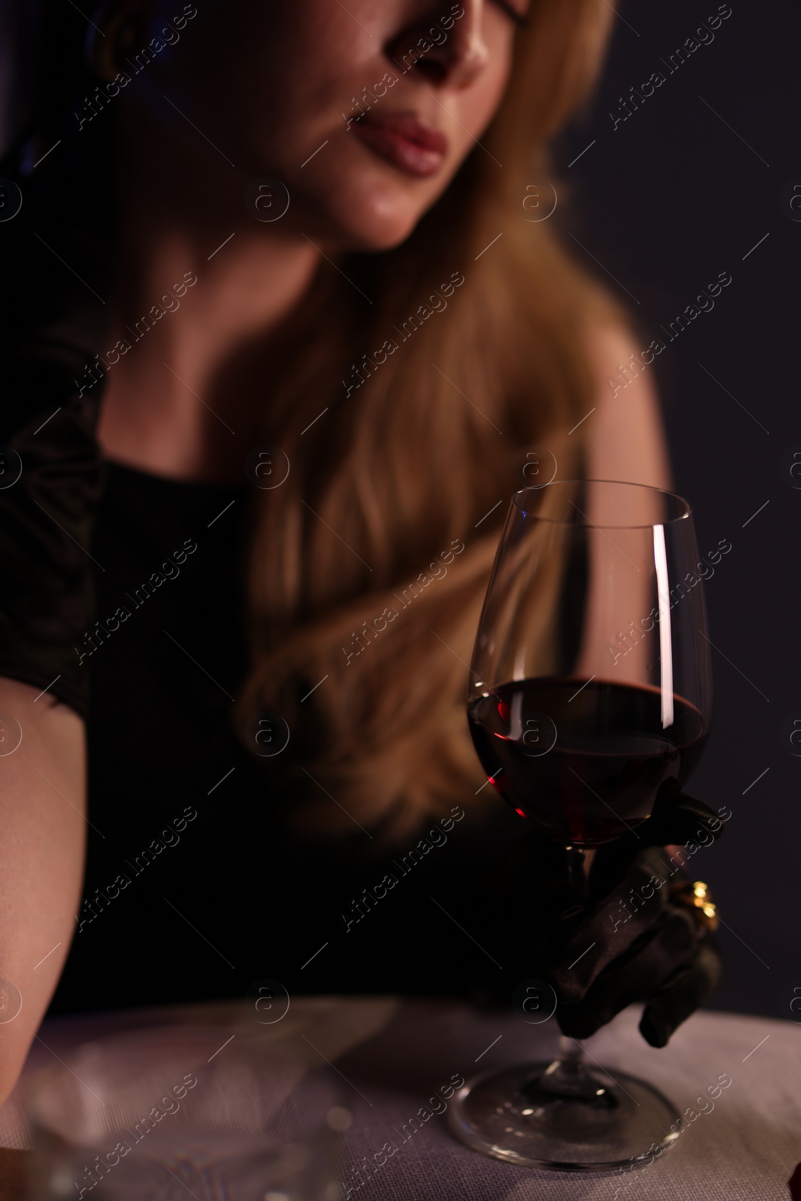 Photo of Elegant young woman with glass of wine at table indoors in evening, closeup