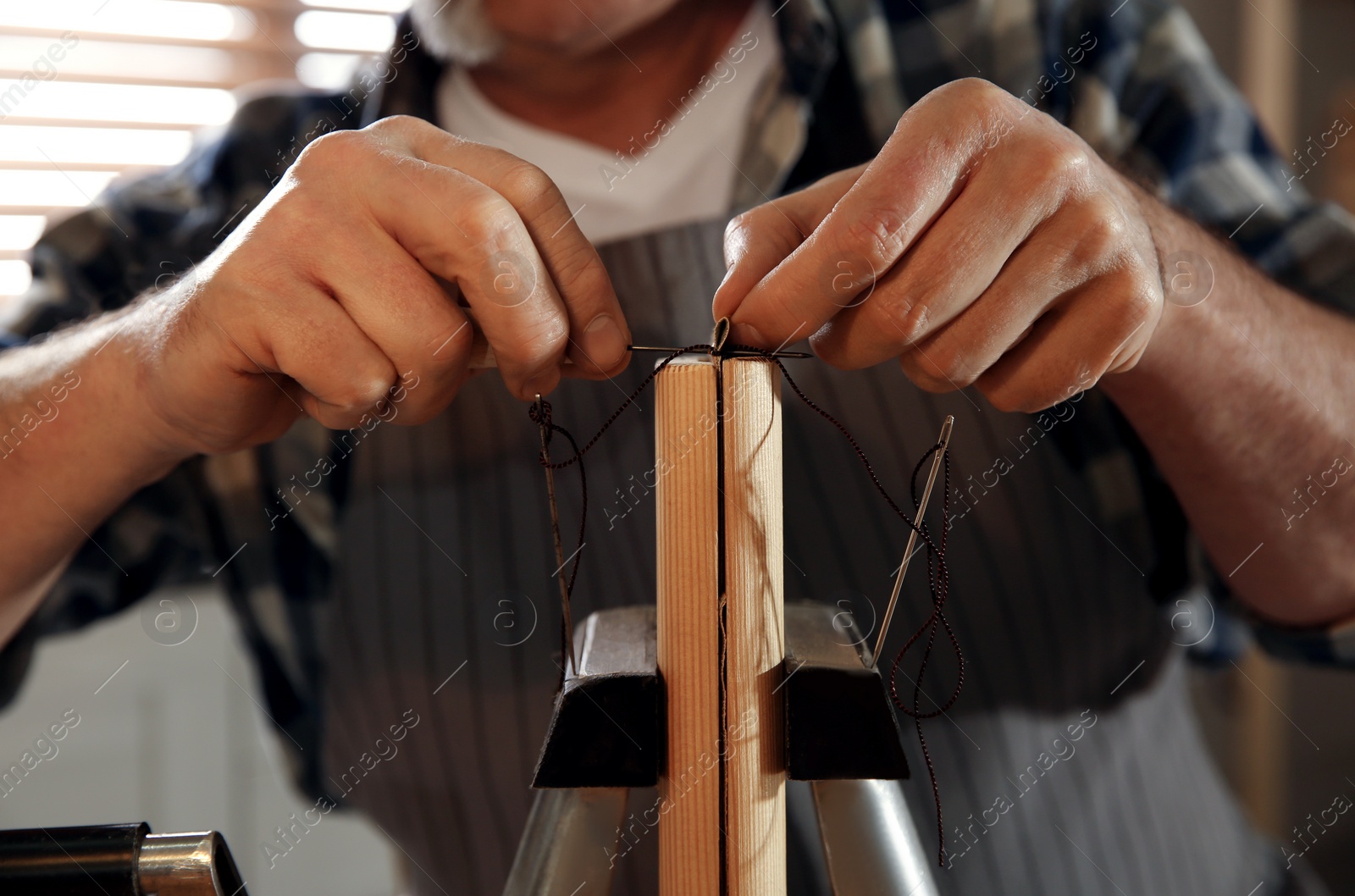 Photo of Man sewing piece of leather in workshop, closeup