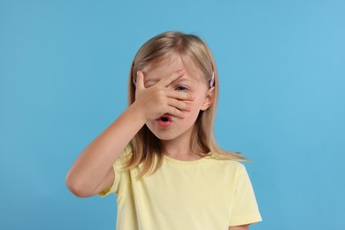 Photo of Embarrassed little girl covering face on light blue background