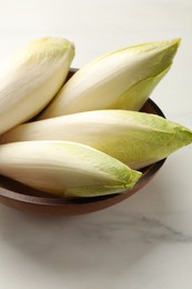 Raw ripe chicories in bowl on white marble table, closeup